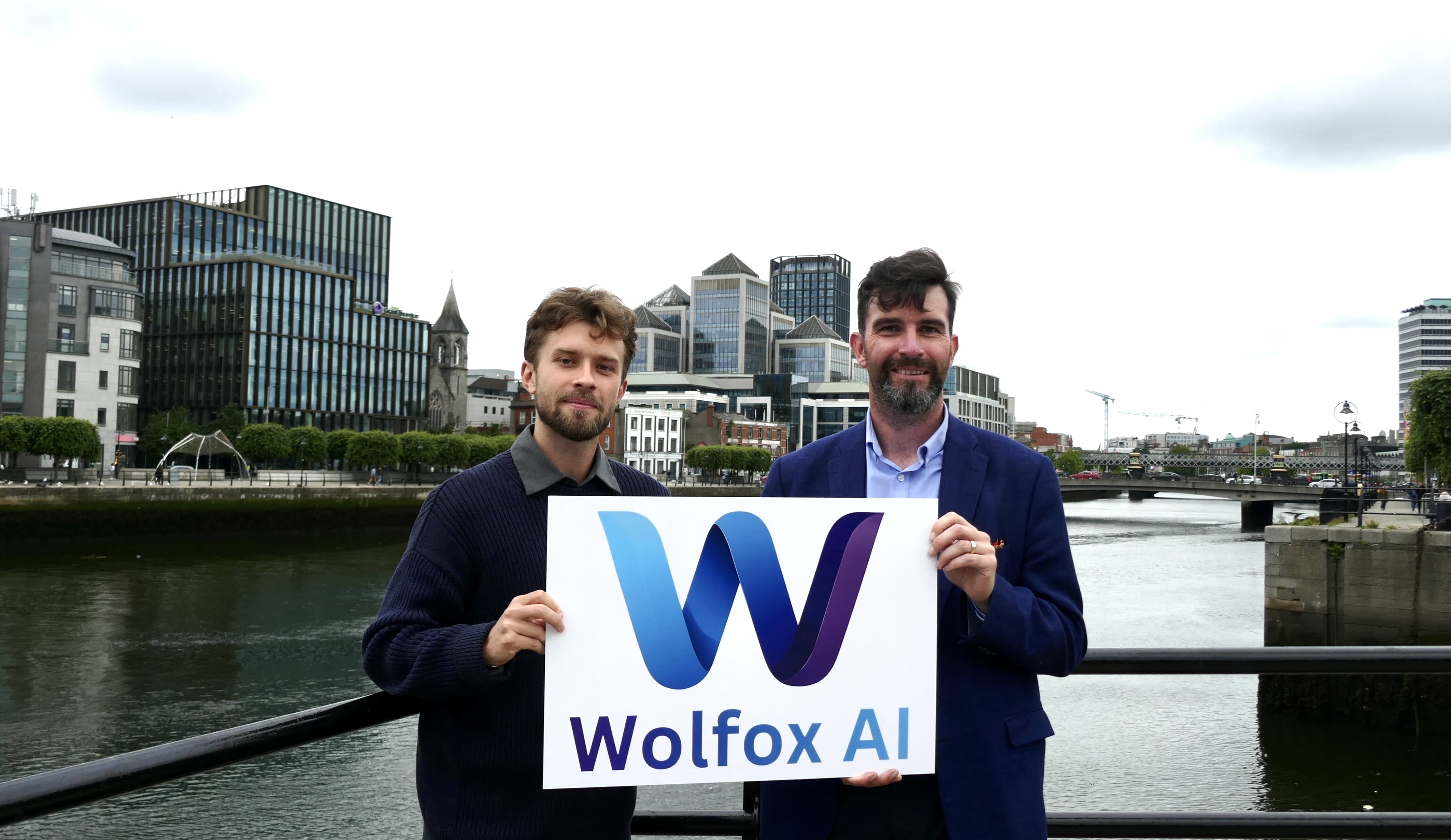 Misha and Leo holding the Wolfox AI logo by the River Liffey in Dublin's IFSC